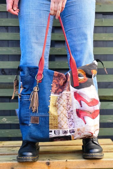 A patchwork tote bag with red handles, worn by a person in denim jeans.