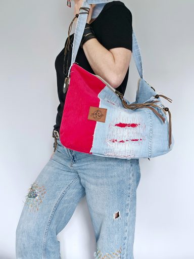 Denim bag with red accents and distressed details, worn by a person in casual jeans.