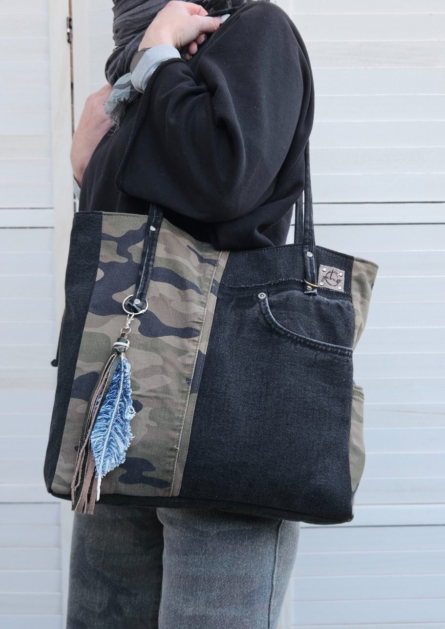 Black Denim Tote Bag Black denim tote bag worn on the shoulder, made from reclaimed jeans with visible pocket detail.