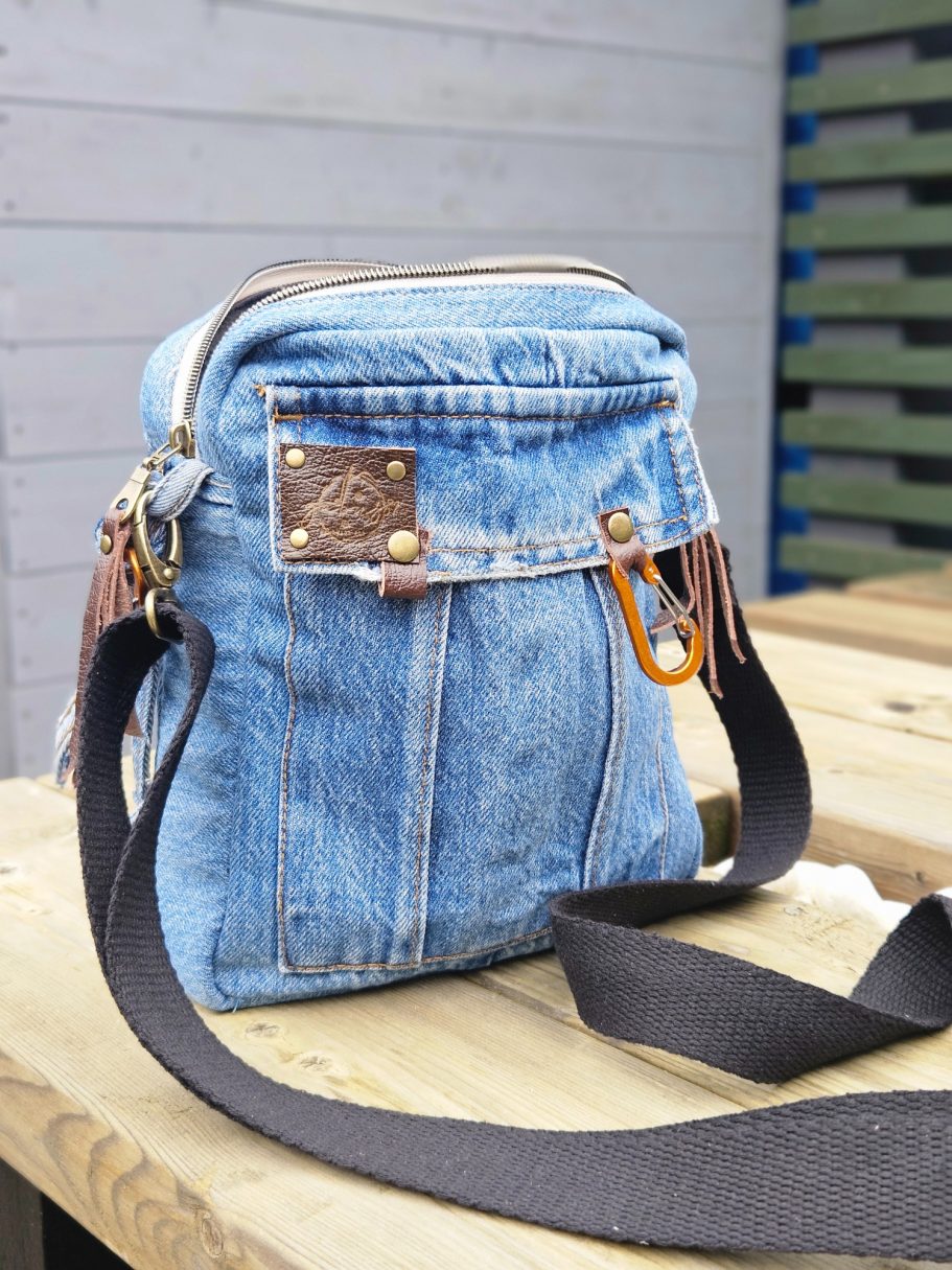 Blue denim crossbody bag with leather accents and a grey strap, set on a wooden surface.