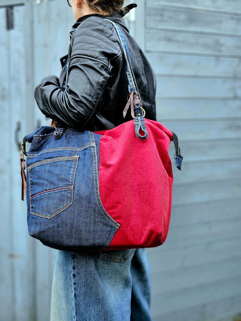 A person carrying a large bag with blue denim and red fabric sections.