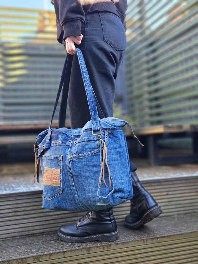 Upcycled Denim Tote Bag Person walking with a large denim tote bag and black boots on wooden steps.