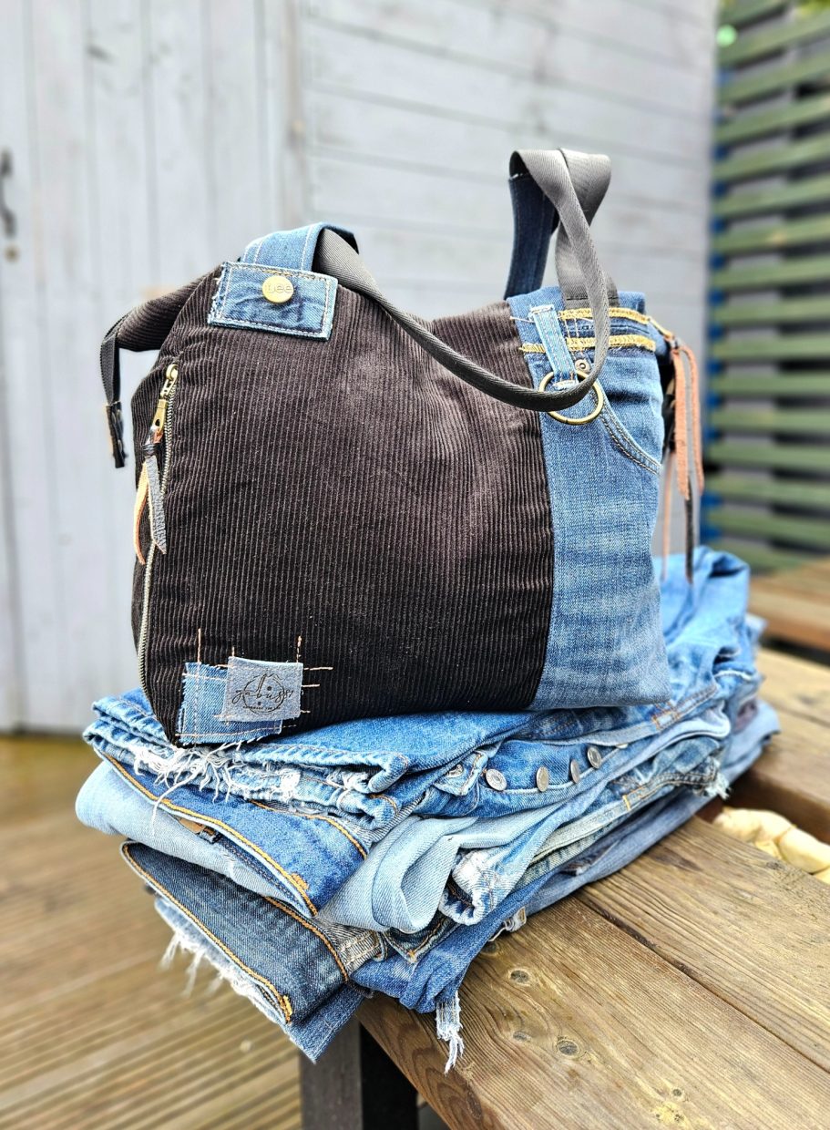 A handbag made from mixed denim and corduroy, resting on a stack of jeans.