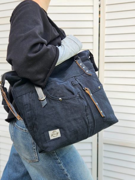 Black Everyday Denim Tote Black everyday denim tote worn on the shoulder, showing its roomy shape and useful front pocket details.