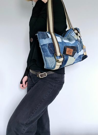 A person wearing a black top and jeans, holding a patchwork denim handbag.