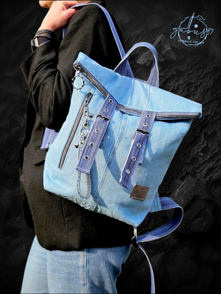 Blue denim backpack Blue denim backpack with adjustable straps and decorative stitching, worn by a person.